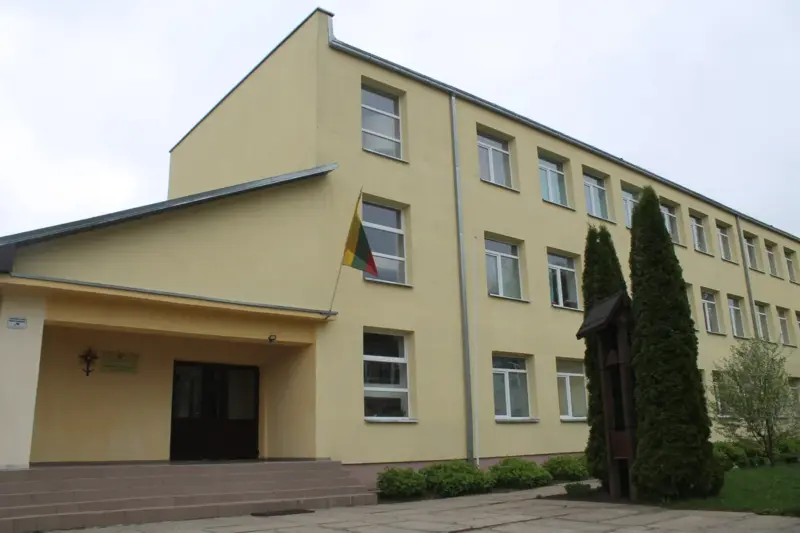 Уваход у мясцовую гімназію, размешчаны за некалькі дзясяткаў метраў ад будынка, дзе ў 2021 годзе планавалася размясціць лагер для бежанцаў. Кідаецца ў вочы кантраст паміж «закінушкай» і дзеючай гімназіяй. Будынак гімназіі прайшоў капітальны рамонт, пафарбаваны ў «жыццярадасны» жоўты колер, тэрыторыя каля гімназіі аблароджана — высаджаны туі, усталявана сучасная дзіцячая пляцоўка. Фота: Hrodna.life