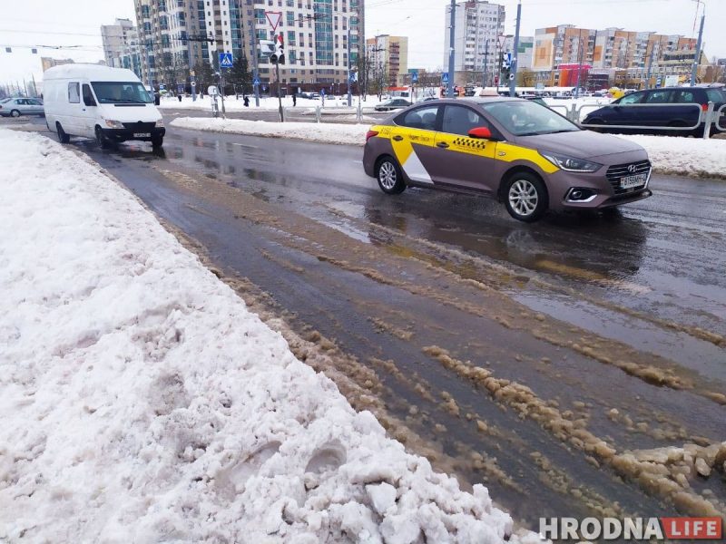 Як зэканоміць на таксі ў навагоднюю ноч Па заснежанай вуліцы з бруднай слотай праязджаюць машыны і зрэдку таксі, а на заднім плане вымалёўваюцца жылыя дамы. Гэта сцэна, якая адлюстроўвае кіпучую энергію навагодняй ночы.