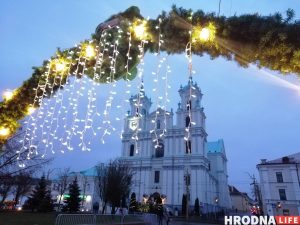 Расіян у Гродне на навагоднія святы будзе больш? Попыт на туры ў Беларусь расце Фарный костел Гродно на Новый год в сумерках, украшенный подвесными гирляндами и зеленью.